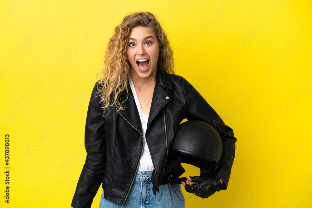 Young blonde woman with a motorcycle helmet isolated on yellow background with surprise facial expression Young blonde woman with a motorcycle helmet isolated on yellow background with surprise facial expression