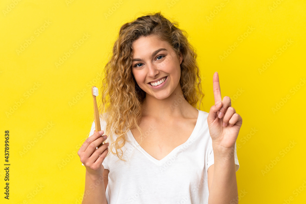 Young caucasian woman holding a brushing teeth isolated on yellow background showing and lifting a finger in sign of the best Young caucasian woman holding a brushing teeth isolated on yellow background showing and lifting a finger in sign of the best