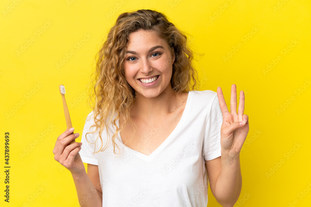 Young caucasian woman holding a brushing teeth isolated on yellow background happy and counting three with fingers Young caucasian woman holding a brushing teeth isolated on yellow background happy and counting three with fingers