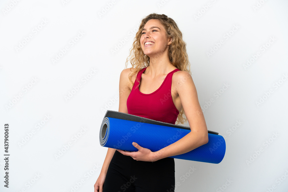 Young sport blonde woman going to yoga classes while holding a mat isolated on white background laughing in lateral position Young sport blonde woman going to yoga classes while holding a mat isolated on white background laughing in lateral position