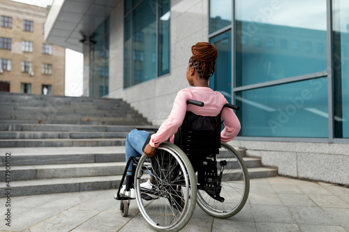 Young black impaired lady in wheelchair cannot go up stairs without ramp, feeling limited and unhappy, copy space