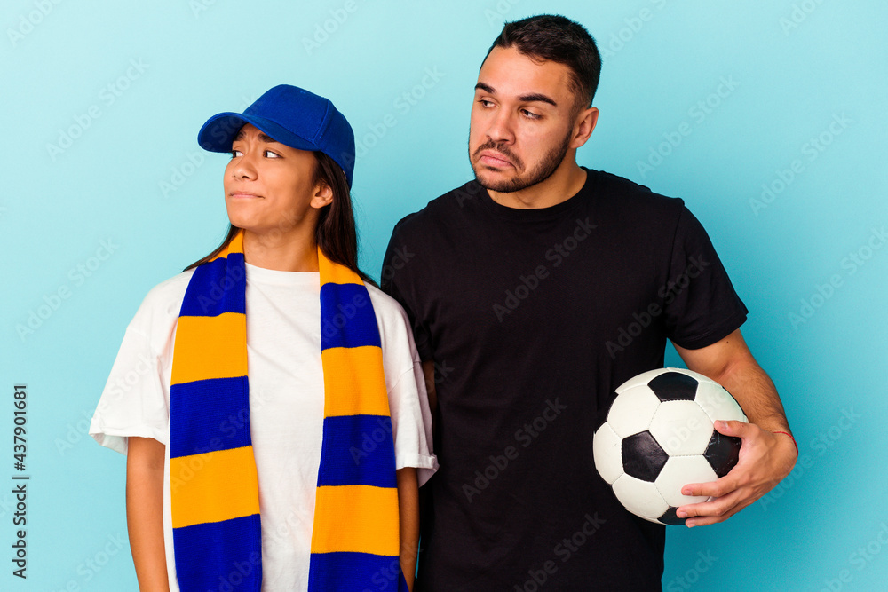 Young mixed race couple cleaning home isolated on blue background confused, feels doubtful and unsure. Young mixed race couple cleaning home isolated on blue background confused, feels doubtful and unsure.