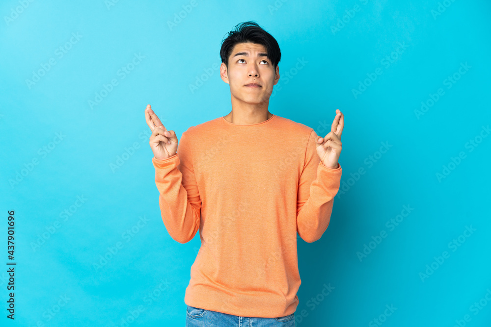 Young Chinese man isolated on blue background with fingers crossing and wishing the best Young Chinese man isolated on blue background with fingers crossing and wishing the best