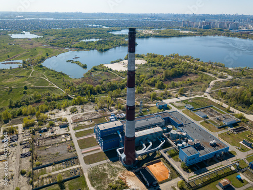 High chimney of a power plant on the outskirts of the city. Green spring steppe on the background. Aerial drone view. photo