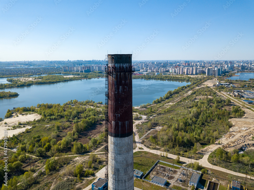 High chimney of a power plant on the outskirts of the city. Green spring steppe on the background. Aerial drone view. High chimney of a power plant on the outskirts of the city. Green spring steppe on the background. Aerial drone view.