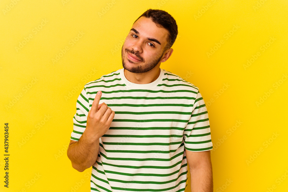 Young caucasian man isolated on yellow background pointing with finger at you as if inviting come closer. Young caucasian man isolated on yellow background pointing with finger at you as if inviting come closer.