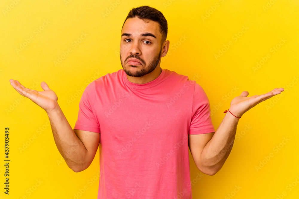 Young caucasian man isolated on yellow background confused and doubtful shrugging shoulders to hold a copy space. Young caucasian man isolated on yellow background confused and doubtful shrugging shoulders to hold a copy space.