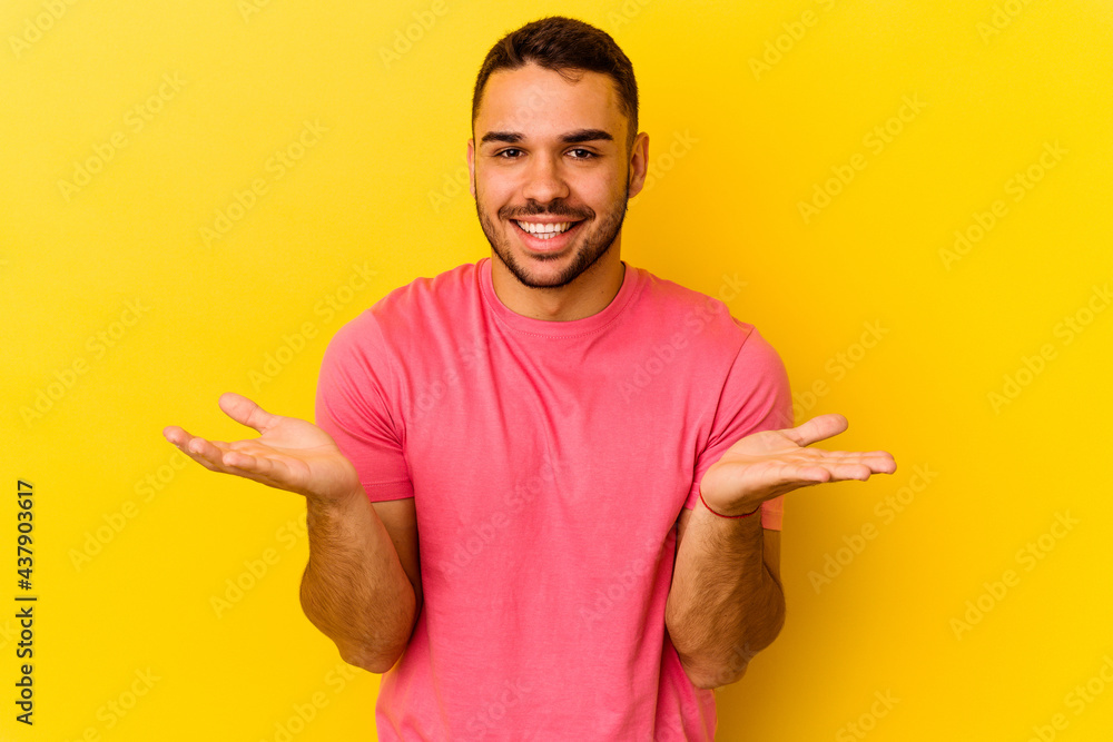 Young caucasian man isolated on yellow background makes scale with arms, feels happy and confident. Young caucasian man isolated on yellow background makes scale with arms, feels happy and confident.