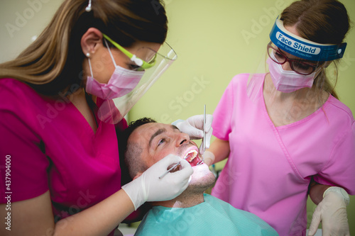 A doctor,dentist,examines the teeth of a younger man in a dental office.