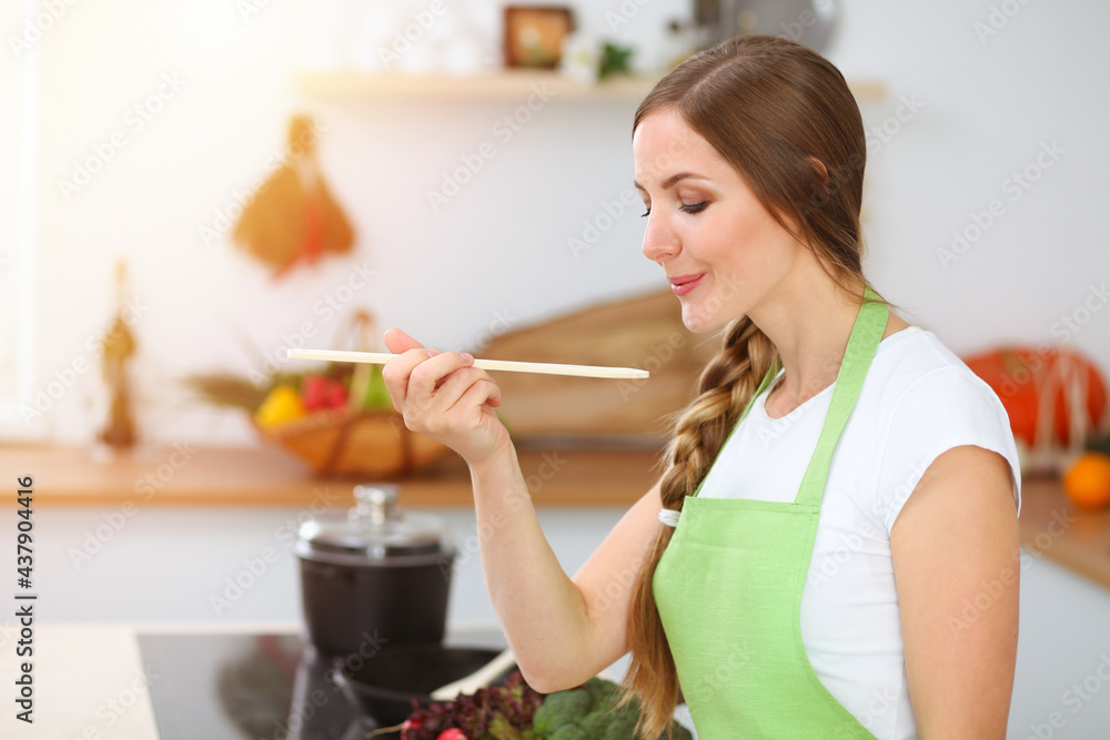 An attractive young woman preparing soup by new keto recipe while standing and smiling in sunny kitchen. Cooking and householding concepts
