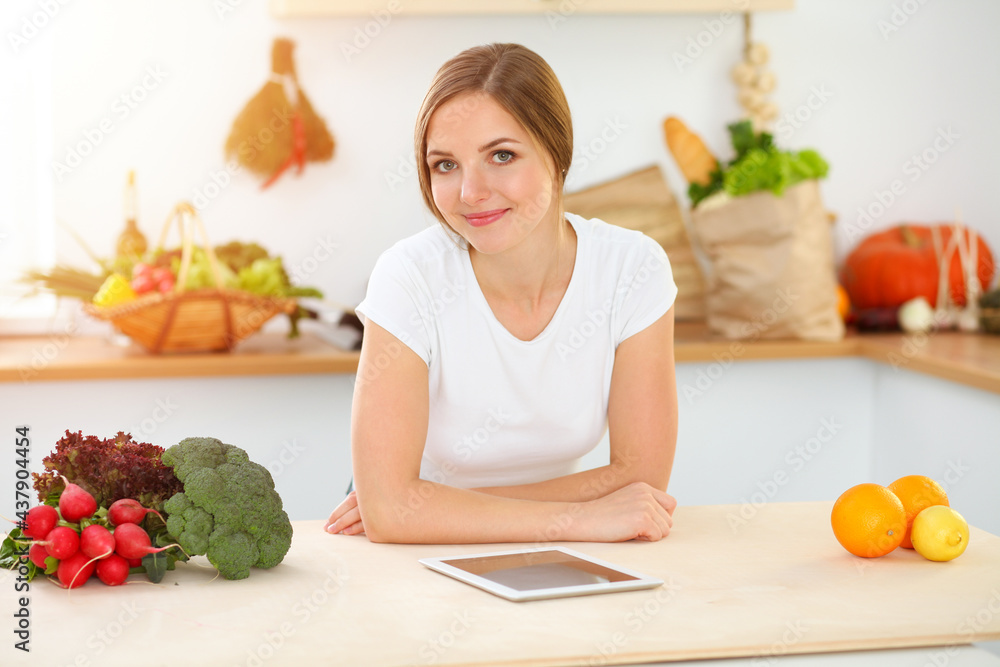 An attractive young woman looking for a new recipe for a delicious salad mix while sitting at the table in sunny kitchen. Tablet pc is the best cookbook An attractive young woman looking for a new recipe for a delicious salad mix while sitting at the table in sunny kitchen. Tablet pc is the best cookbook