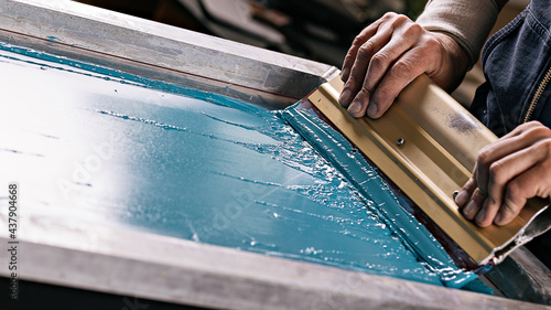 selective focus photo of male hands with squeegee. serigraphy production. printing images on t-shirts by silkscreen method in a design studio photo