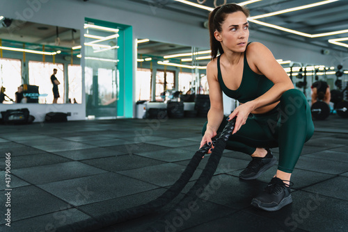 White sportswoman doing workout with battle ropes in gym