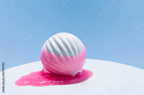 Modern contemporary abstract composition - metaphor of overflow glamour fashion. Pink slime with glitter flow down of white vase on white wood table, soft light blue wall. photo