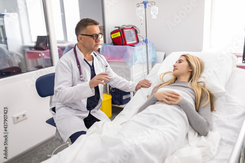 Mature man doctor reassuring his female patient in bed at hospital. Medical ethics and trust concept.