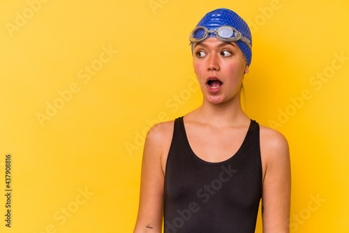 Young swimmer venezuelan woman isolated on yellow background being shocked because of something she has seen. © Asier