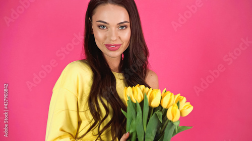 smiling young adult woman holding bouquet of tulips isolated on pink