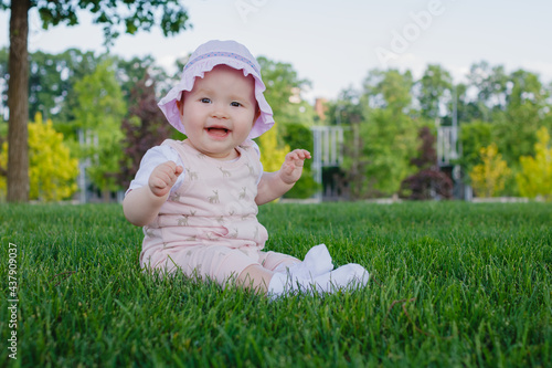 Cute 8 months old newborn nursing baby girl sitting on the grass in the park and smiling on a summer sunny day. Place for text.