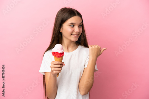 Little girl with a cornet ice cream over isolated pink background pointing to the side to present a product