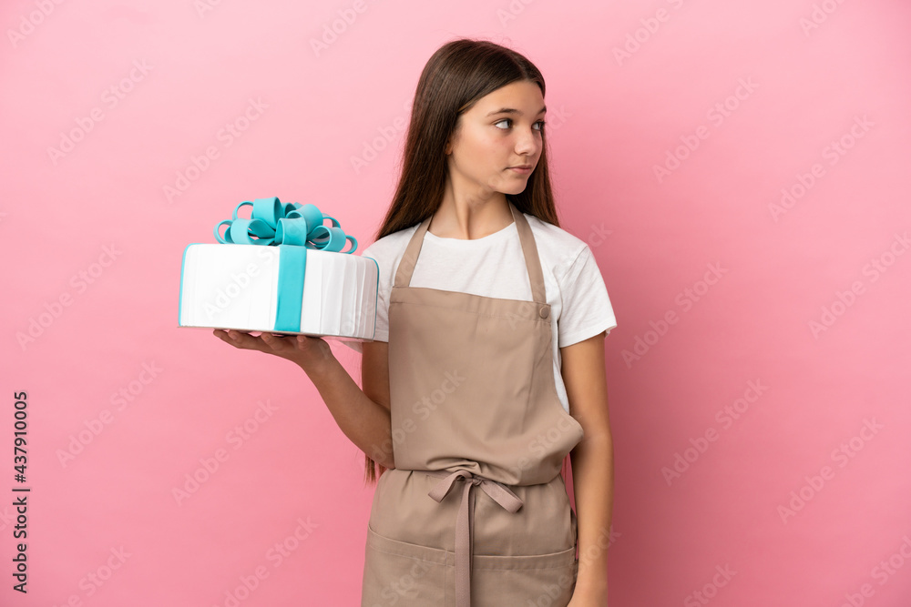 Little girl with a big cake over isolated pink background looking to the side Little girl with a big cake over isolated pink background looking to the side