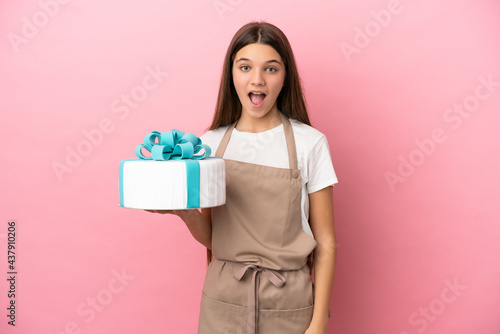 Little girl with a big cake over isolated pink background with surprise facial expression