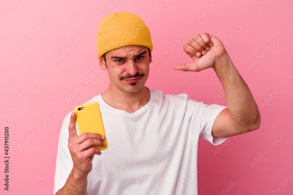 Young caucasian man holding a mobile phone isolated on pink background feels proud and self confident, example to follow. Young caucasian man holding a mobile phone isolated on pink background feels proud and self confident, example to follow.