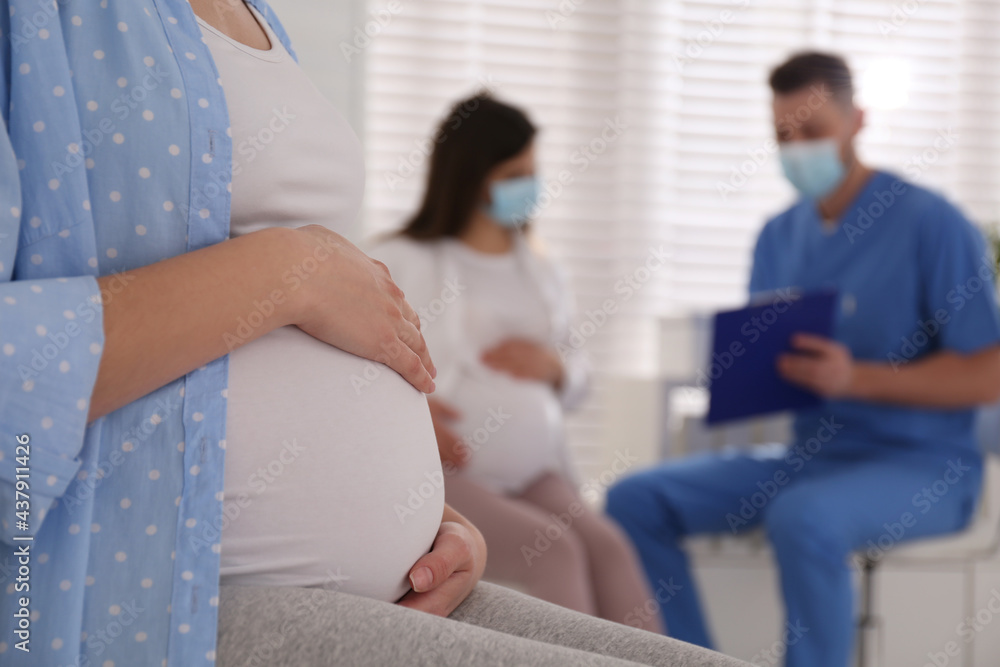 Fototapeta premium Pregnant woman waiting for appointment while doctor consulting other patient in clinic, focus on belly