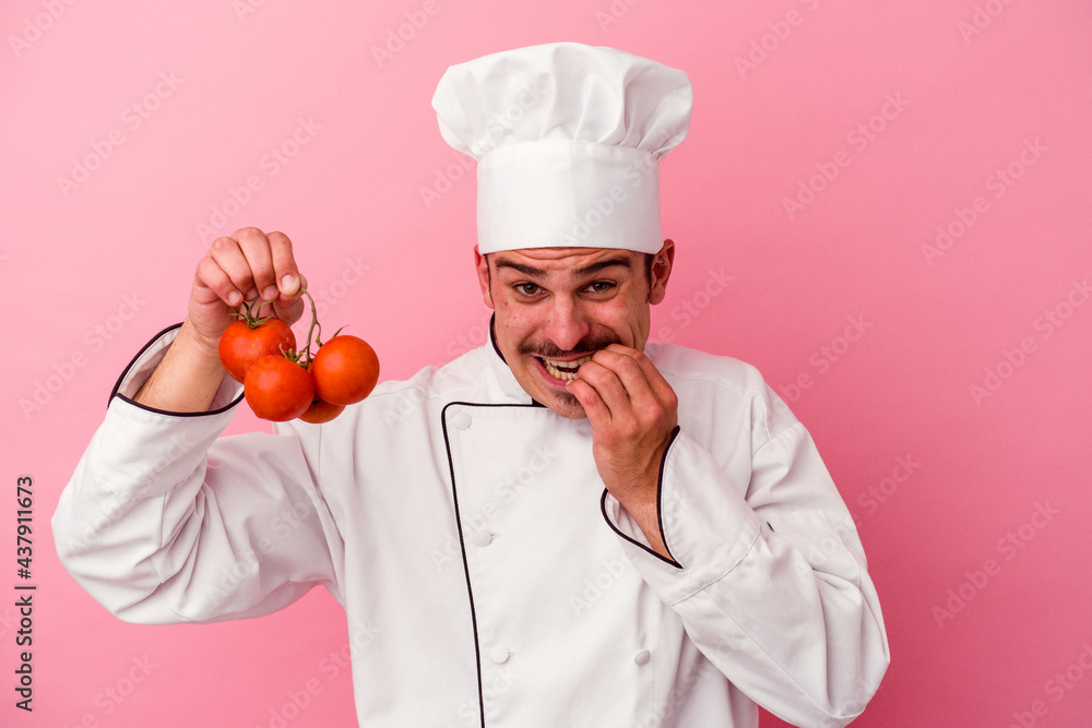 Young caucasian chef man holding tomatoes isolated on pink background biting fingernails, nervous and very anxious. Young caucasian chef man holding tomatoes isolated on pink background biting fingernails, nervous and very anxious.