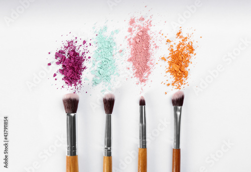 Makeup brushes and scattered eye shadows on white background, flat lay