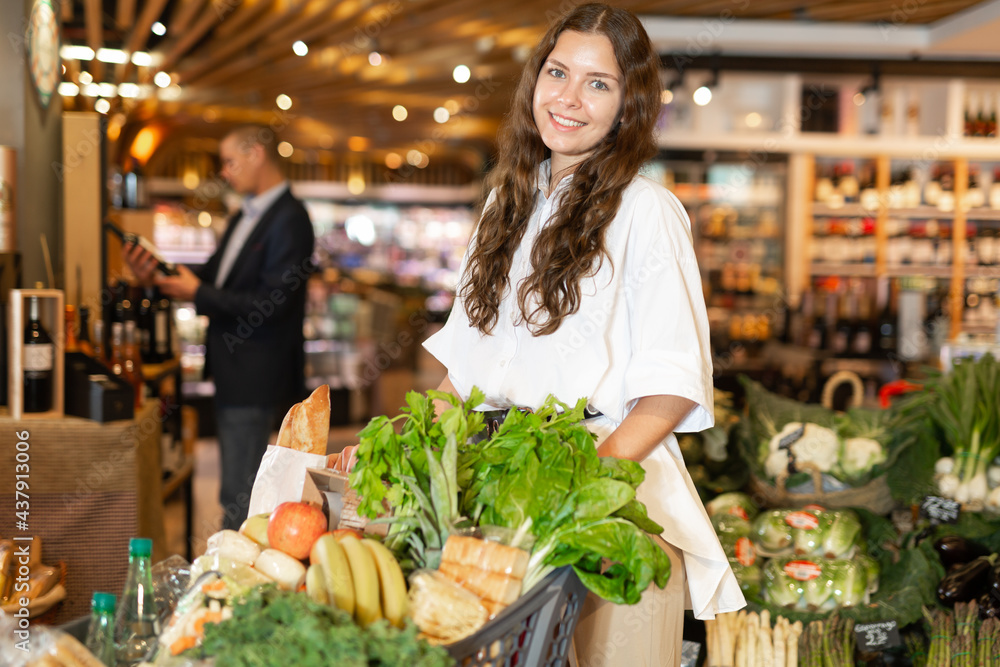 Positive young woman with shopping cart at grocery supermarket