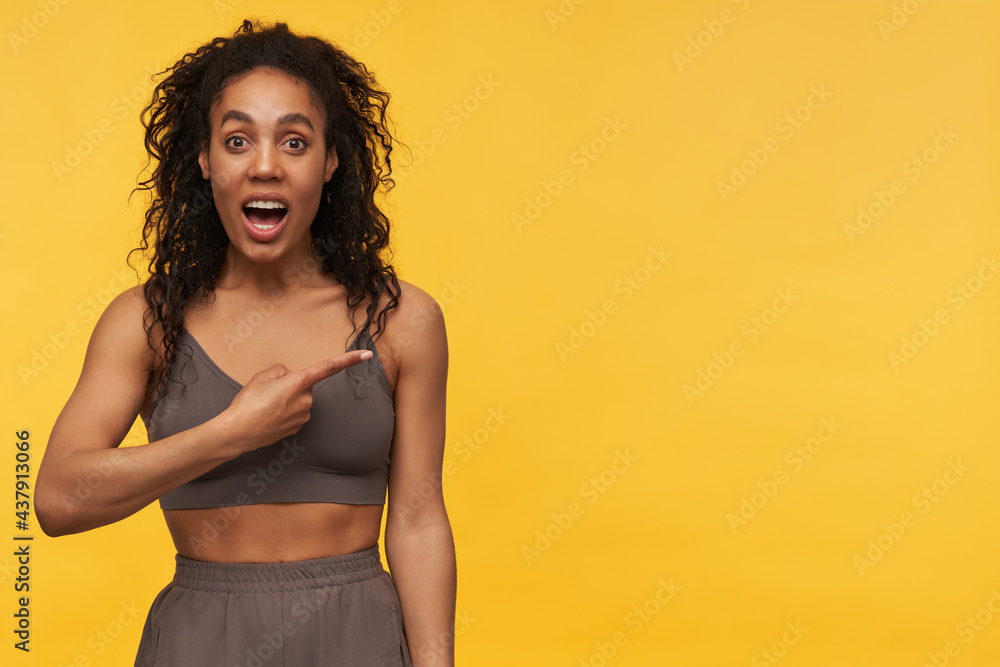Amazed pretty african american young fitness woman with opened mouth looks shocked and pointing away to the side at copyspace isolated over yellow background Amazed pretty african american young fitness woman with opened mouth looks shocked and pointing away to the side at copyspace isolated over yellow background