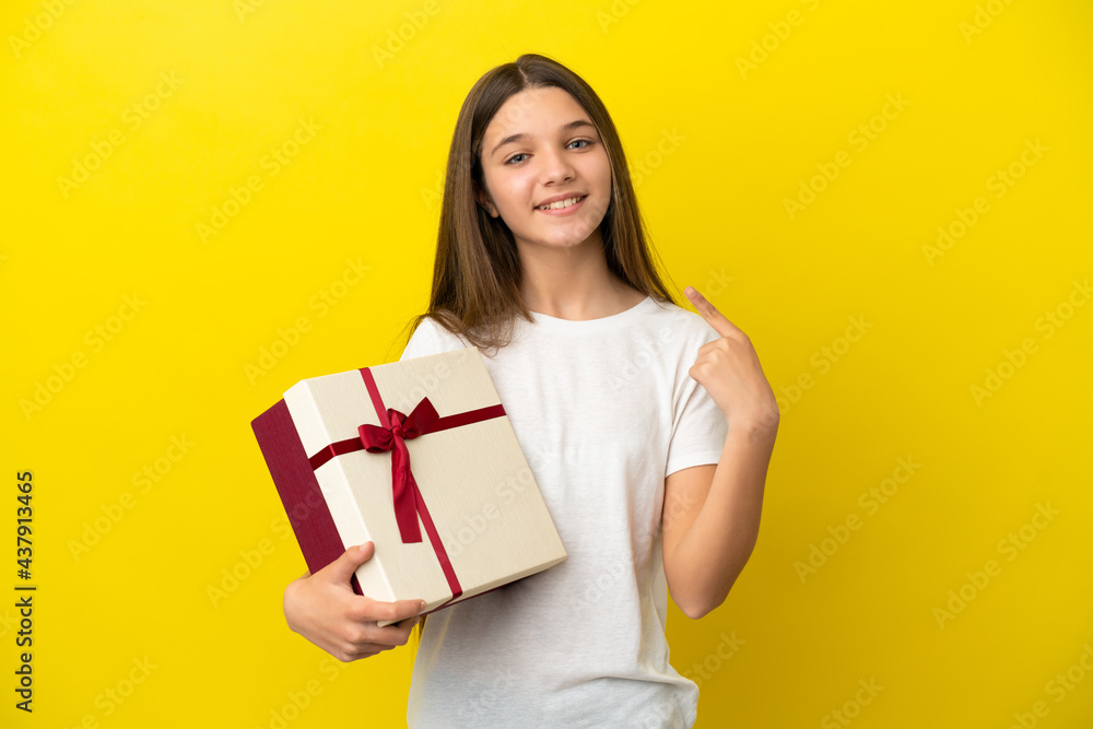 Little girl holding a gift over isolated yellow background giving a thumbs up gesture Little girl holding a gift over isolated yellow background giving a thumbs up gesture