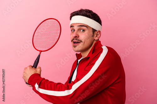 Young caucasian man playing badminton isolated on pink background © Asier