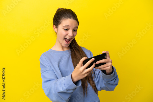 Little girl over isolated yellow background playing with the mobile phone