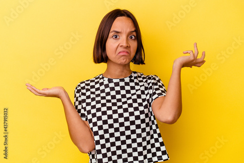 Young mixed race woman isolated on yellow background confused and doubtful shrugging shoulders to hold a copy space.