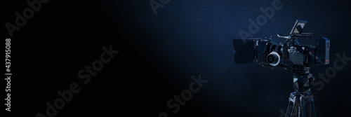 Digital film camera in the dark on blue concrete wall background. Video camera with copy space for film production, tv or broadcast media banner.