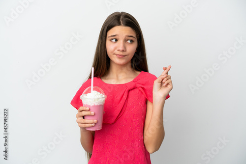 Little girl with strawberry milkshake over isolated white background with fingers crossing and wishing the best