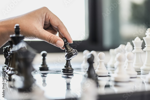 A businesswoman holding a black chess piece walks forward on a chessboard, comparing the chessboard to business administration, planning operations to achieve goals and solve business problems.
