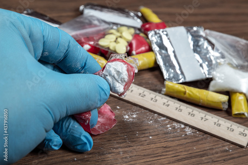 evidence of smuggling traffic: Packaging of a narcotic substance in the hand of a forensic expert against the background of other arrested materials, cocaine, heroin, spice