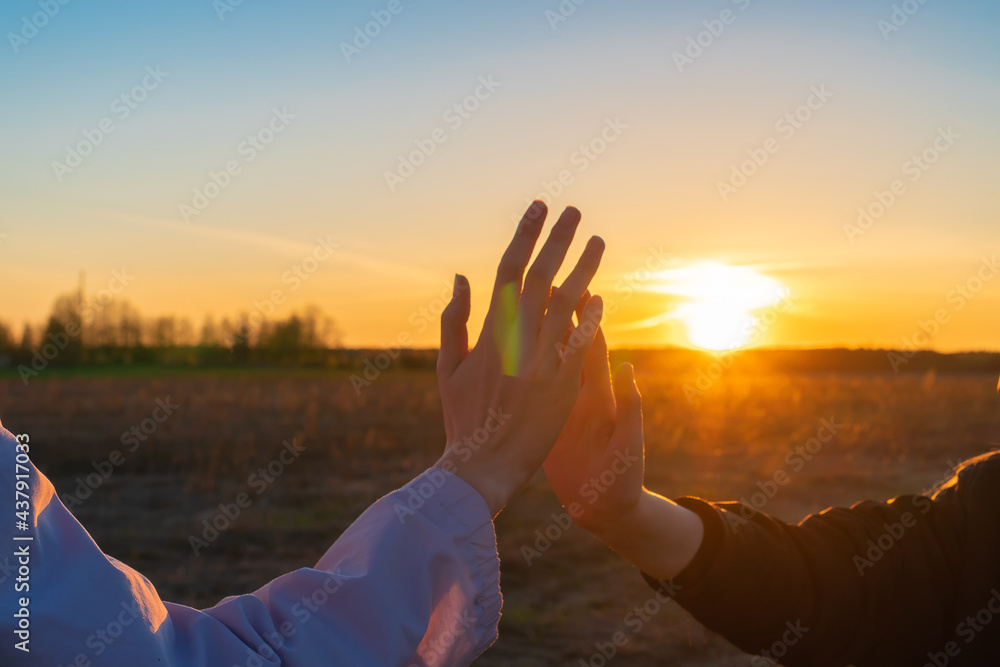 Fototapeta premium Female hand meets female teen hand against sky and sunset background close-up, copy space