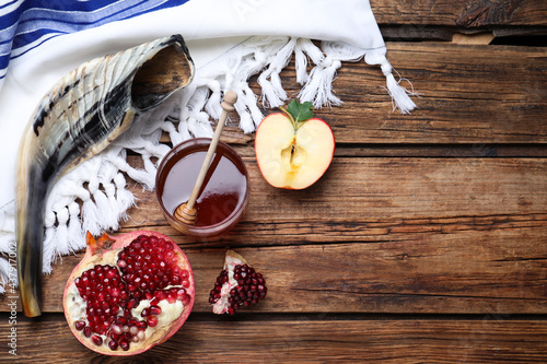 Honey, pomegranate, apples and shofar on wooden table, flat lay with space for text. Rosh Hashana holiday photo