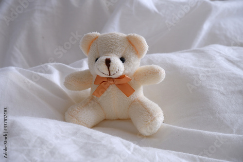Beige teddy bear on a white bed.