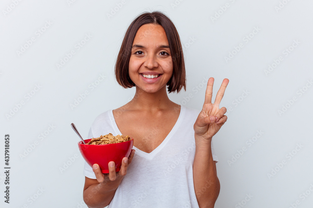 Young mixed race woman eating cereals isolated on white background showing number two with fingers. Young mixed race woman eating cereals isolated on white background showing number two with fingers.