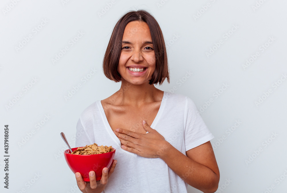 Young mixed race woman eating cereals isolated on white background laughs out loudly keeping hand on chest. Young mixed race woman eating cereals isolated on white background laughs out loudly keeping hand on chest.