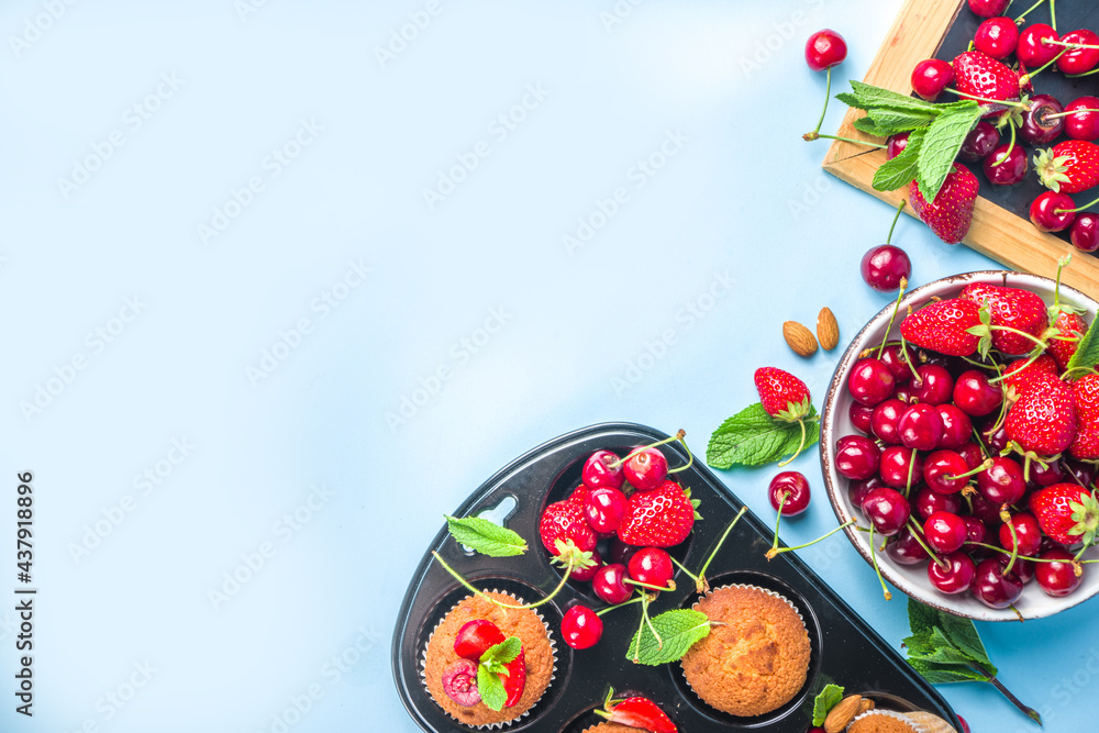 Summer baking concept, homemade vanilla white muffins with berry - strawberry, cherry, and mint, on baking sheet, light blue background top view copy space
