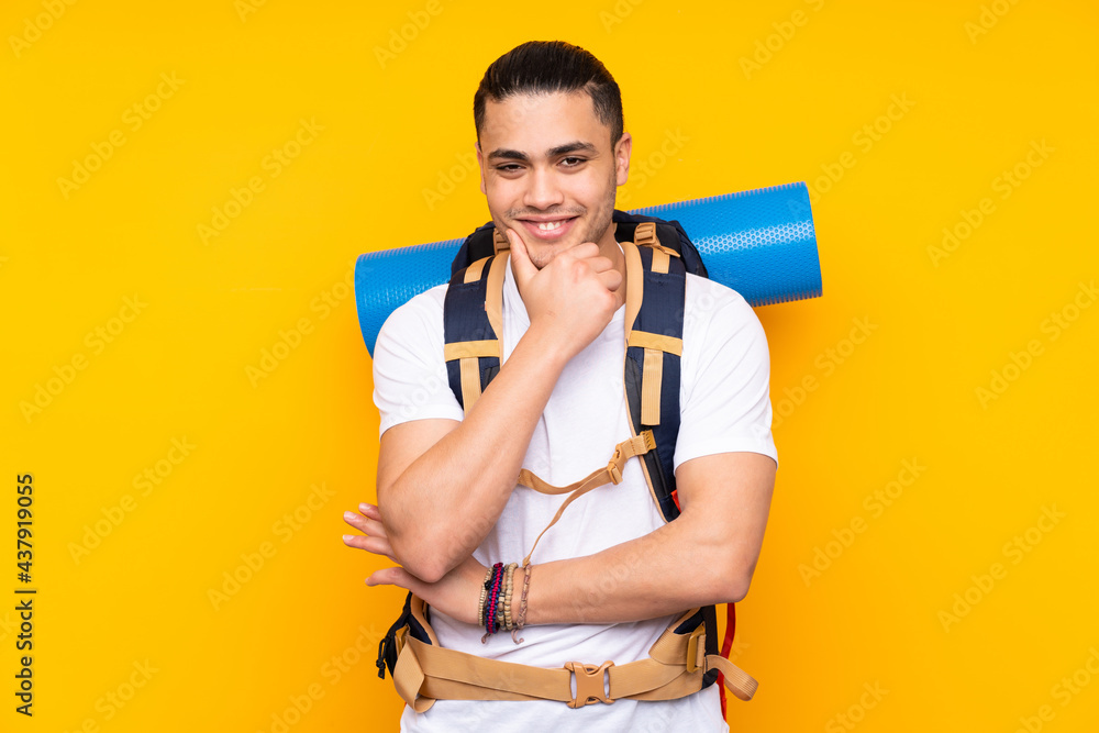 Young mountaineer asian man with a big backpack isolated on yellow background laughing Young mountaineer asian man with a big backpack isolated on yellow background laughing