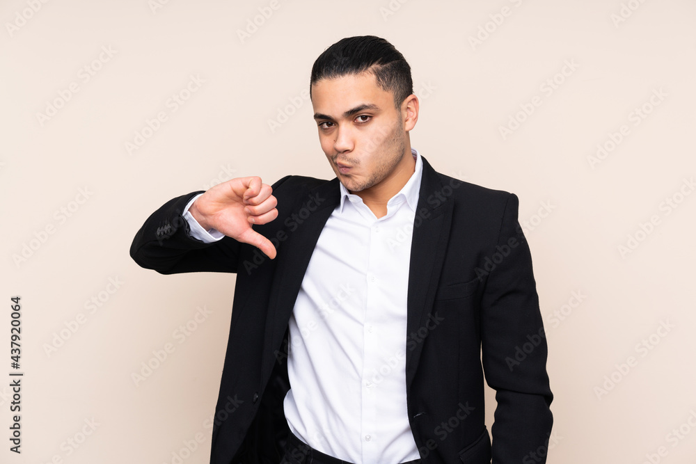Asian business man isolated on beige background showing thumb down sign Asian business man isolated on beige background showing thumb down sign