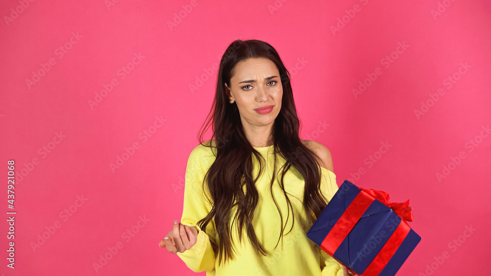 dissatisfied young adult woman holding gift box with gesturing with hand isolated on pink dissatisfied young adult woman holding gift box with gesturing with hand isolated on pink