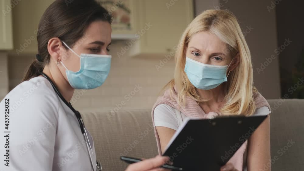 woman doctor help middle aged woman during homecare medical visit with mask on face, female doctor talk with 40s patient give empathy support and prescribes treatment while sitting on sofa at home woman doctor help middle aged woman during homecare medical visit with mask on face, female doctor talk with 40s patient give empathy support and prescribes treatment while sitting on sofa at home