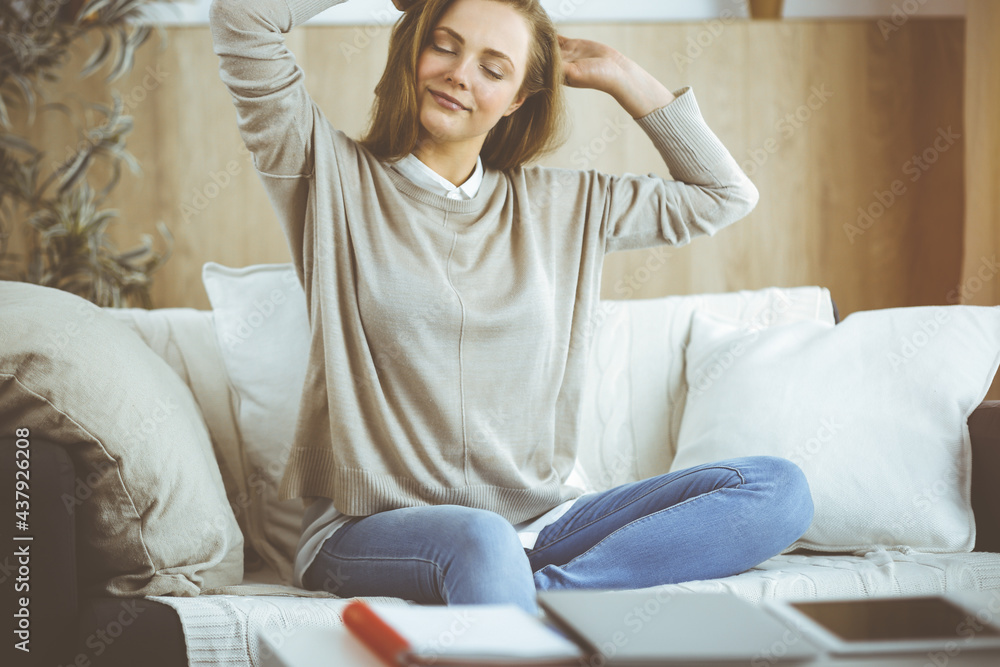 Happy brunette woman put hands behind head sitting leaned on couch, european female stretching and enjoying lazy weekend or vacation in cozy living room Happy brunette woman put hands behind head sitting leaned on couch, european female stretching and enjoying lazy weekend or vacation in cozy living room